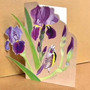 May include: A hand-painted card featuring a purple iris flower with a yellow center and a small yellow and black bird singing. The card is on a brown background with green leaves.