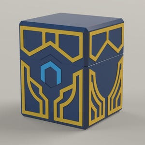 Könnte beinhalten: Eine blaue Box mit goldenen geometrischen Designs. Die Box hat einen sechseckigen blauen Akzent und goldene Verzierungen. Die Box hat eine Würfelform und einen Deckel. Die Box ist wahrscheinlich für die Aufbewahrung oder Präsentation gedacht.