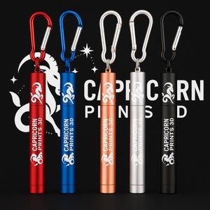 Könnte beinhalten: Fünf zylindrische Metallbehälter mit Karabinerhaken in Rot, Blau, Kupfer, Silber und Schwarz. Jeder Behälter hat ein Steinbock-Sternzeichen und den Text "CAPRICORN PRINTS 3D".