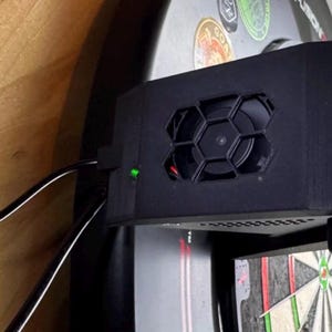 Peut inclure: Un dispositif de refroidissement électronique noir et rectangulaire doté d'un ventilateur circulaire central protégé par une grille hexagonale. L'unité présente un petit voyant LED vert allumé et deux câbles d'alimentation noirs sur le côté.