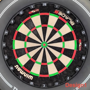 Puede incluir: Un tablero de dardos negro con un diseño circular, con secciones beige y negras alternas. El tablero tiene anillos rojos y verdes, con números alrededor del perímetro. Los textos "WINMAU" y "BLADE 6" son visibles. El diseño está etiquetado como "Design 1".