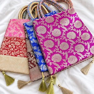 May include: A collection of four square handbags featuring vibrant silk-like fabric with intricate floral patterns in magenta, blue, red, and pink. Each bag includes braided multi-colored handles and a dangling beige tassel at the bottom corner.