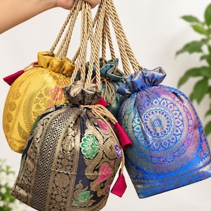 May include: A collection of four drawstring pouches featuring intricate woven patterns in yellow, black, blue, and teal. Each bag is crafted from fabric with metallic gold accents and includes twisted gold rope handles and small pink fabric tassels.