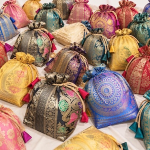 Puede incluir: Una colección de bolsas con cordón hechas de tela de brocado multicolor con intrincados patrones florales y geométricos. Cada bolsa se cierra con cordones dorados trenzados que terminan en pequeñas borlas de tela, en colores como oro, azul, rojo, rosa y turquesa.