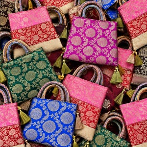 May include: A collection of square fabric handbags featuring intricate floral brocade patterns in vibrant colors including pink, red, green, and blue. Each bag has braided handles and decorative tassels attached to the base of the handles.