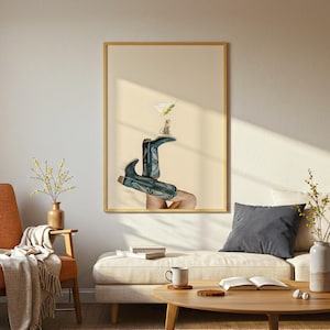 May include: A framed art print featuring a surreal composition. Teal cowboy boots are positioned to support a martini glass with olives and a small animal figure. The background is a soft beige.