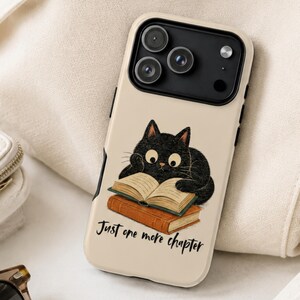 May include: A beige smartphone case featuring a black cat with large eyes reading an open book resting on a closed brown book. Below the illustration, the text reads Just one more chapter in a black cursive font. The case has a black camera module.