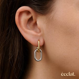 Puede incluir: Un pendiente de eslabón de cadena dorado y plateado se muestra en una oreja. El pendiente tiene un aro dorado que se conecta a un eslabón ovalado plateado. La palabra "éclat" está en la esquina inferior derecha.