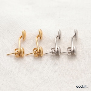 May include: Two pairs of stud earrings, one pair in gold tone and one pair in silver tone. Each earring features a curved, elongated metal bar with a smooth, rounded end and a standard post back. The word "écclat." is printed in the bottom right corner.
