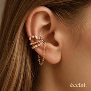 Peut inclure: Ensemble de manchettes d'oreille dorées avec trois pièces. La manchette supérieure présente un design géométrique avec de petites pierres transparentes. La manchette du milieu a un design perlé avec de petites pierres transparentes.