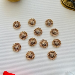 May include: Eleven circular gold-toned metal buttons arranged in a cluster. Each button features a sunburst pattern radiating from a central point, surrounded by a scalloped edge. The buttons have a metallic finish and a small clear stone in the center.