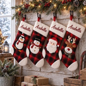 Pode incluir: Quatro meias de Natal com padrão xadrez vermelho e preto e punhos de pele sintética branca. Cada punho tem o nome Arabella bordado em vermelho. As meias apresentam aplicações de pelúcia de um pinguim, boneco de neve, Pai Natal e rena.