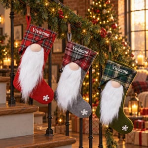 Peut inclure: Trois chaussettes de Noël avec des motifs de gnomes, dotées de longues barbes en fausse fourrure blanche, de nez beiges et de revers à carreaux. Chaque chaussette est personnalisée avec le nom Vivienne brodé en blanc et un flocon de neige.