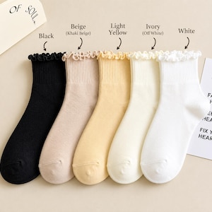 Peut inclure: Cinq paires de chaussettes &agrave; volants de couleurs vari&eacute;es : noir, beige, jaune clair, ivoire et blanc. Les chaussettes sont pr&eacute;sent&eacute;es sur un fond clair. Le texte indique "OF SOUL" et "BE FACE HAPPY FEEL HEART FIX YOUR HEART."