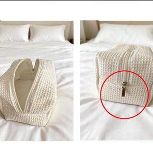May include: A cream-colored rectangular toiletry bag featuring a textured waffle-weave fabric pattern. The bag has a central zipper closure with a metallic pull tab, shown both partially open and fully closed in two separate views.