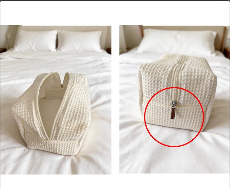 May include: A cream-colored rectangular toiletry bag featuring a textured waffle-weave fabric pattern. The bag has a central zipper closure with a metallic pull tab, shown both partially open and fully closed in two separate views.
