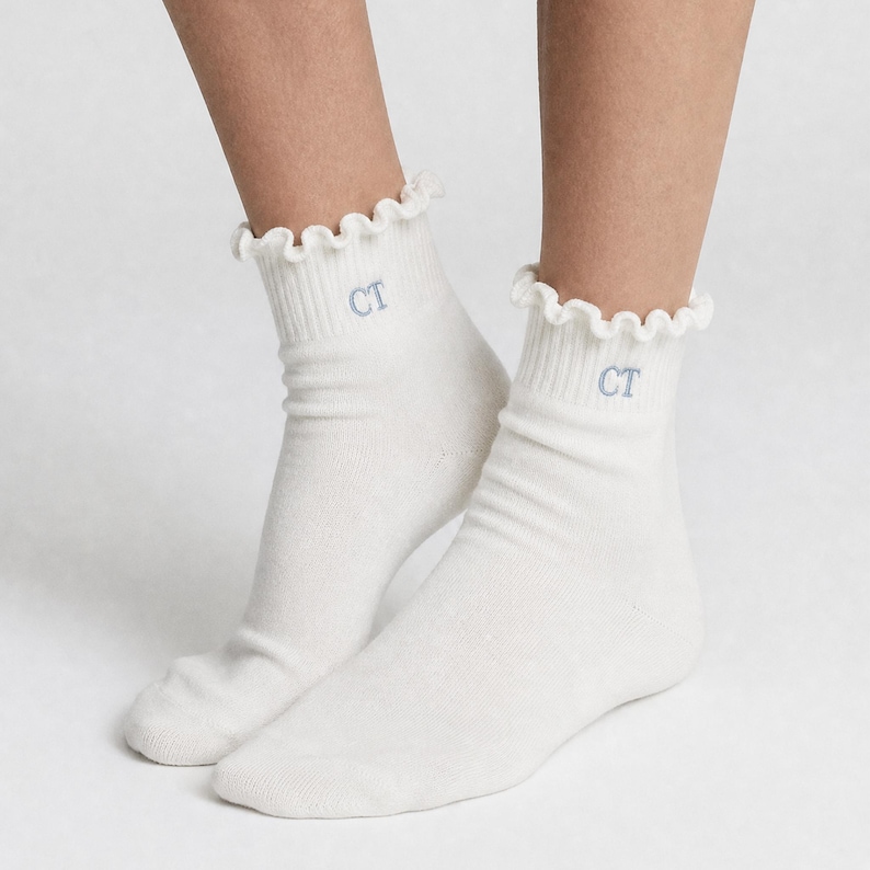 Peut inclure: Une paire de chaussettes courtes blanches avec un bord &agrave; volants. Les chaussettes portent les lettres brod&eacute;es "CT" en bleu clair. Les chaussettes sont en maille c&ocirc;tel&eacute;e douce.
