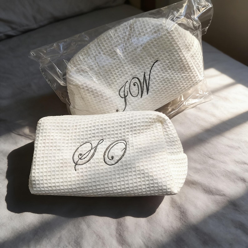 May include: Two white waffle-textured fabric pouches with dark grey embroidered lettering. One pouch is inside a clear plastic bag and features the letters JW, while the other is outside the bag and features the letters SO in a cursive script font.