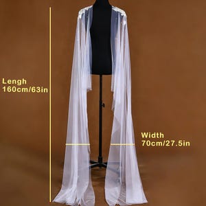 Pu&ograve; includere: Una cappa bianca e trasparente con dettagli di perle e pizzo sulle spalle. La cappa &egrave; esposta su un manichino nero, con una lunghezza di 160 cm e una larghezza di 70 cm. Adatta per occasioni formali.