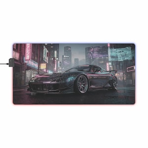 Könnte beinhalten: Rechteckiges, schwarz-graues Gaming-Mauspad mit einer futuristischen Stadtlandschaft und einem dunkelgrauen Sportwagen. Das Pad hat einen leuchtenden rot-blauen Rand und ein schwarzes Netzkabel.