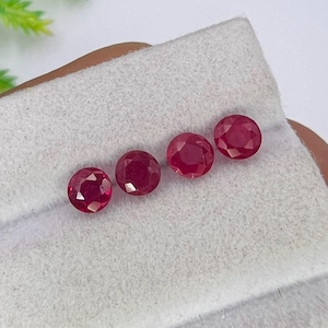 Puede incluir: Cuatro rubíes redondos, facetados y de color rojo intenso están dispuestos en una fila horizontal. Cada piedra preciosa presenta un corte brillante con múltiples facetas triangulares que reflejan la luz, mostrando un tono carmesí vibrante.