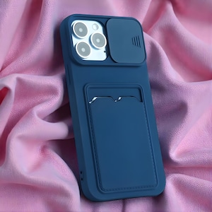 May include: A navy blue phone case with a camera cover and a cardholder. The case has a smooth finish and is designed to protect the phone. The cardholder is located on the back of the case.
