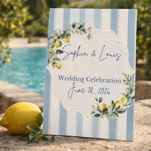 May include: A wedding sign with a blue and white striped background. The sign features the names "Sophia & Louis" and the date "June 18, 2026". Lemon and leaf illustrations decorate the sign. A lemon and greenery are in the foreground.