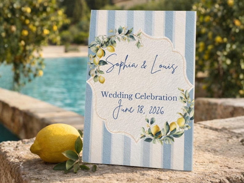 May include: A wedding sign with a blue and white striped background. The sign features the names "Sophia & Louis" and the date "June 18, 2026". Lemon and leaf illustrations decorate the sign. A lemon and greenery are in the foreground.