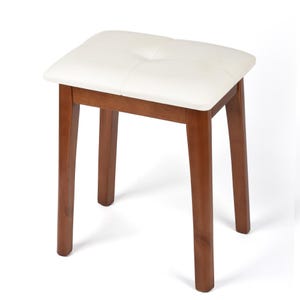 May include: A square vanity stool with a white cushioned seat and four brown wooden legs. The seat has a tufted design. The stool is designed for use in a bedroom or bathroom.