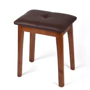 May include: A brown vanity bench with cushion seat, padded seat and four wooden legs. The seat is a dark brown color with a tufted design. The legs are a lighter brown color.