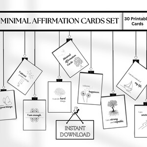 May include: A minimalist black and white set of affirmation cards. The set includes 30 printable cards with positive affirmations, such as "I am enough" and "I attract positive energy." The cards are suspended from a black frame.