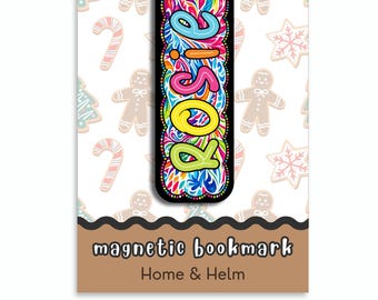 May include: A rectangular magnetic bookmark featuring the name Rosie in colourful, swirling patterns on a black background. The bookmark is displayed on a card with a gingerbread man and candy cane print, labelled magnetic bookmark Home & Helm.