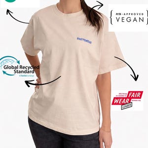 May include: Cream-colored t-shirt with the word "SOSTENELLE" in blue script. The shirt is labeled as PETA-Approved Vegan, OEKO-TEX Standard 100, and Fair Wear Leader, indicating sustainable and ethical production.