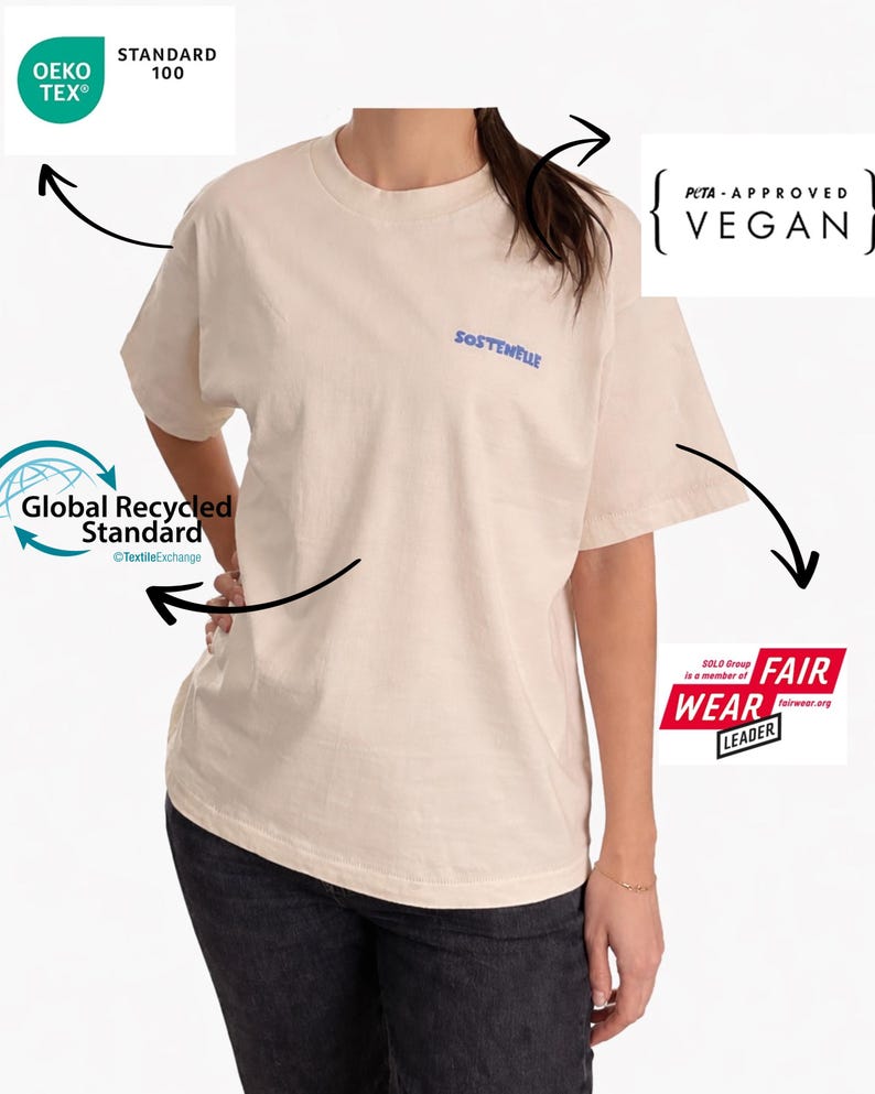 May include: Cream-colored t-shirt with the word "SOSTENELLE" in blue script. The shirt is labeled as PETA-Approved Vegan, OEKO-TEX Standard 100, and Fair Wear Leader, indicating sustainable and ethical production.