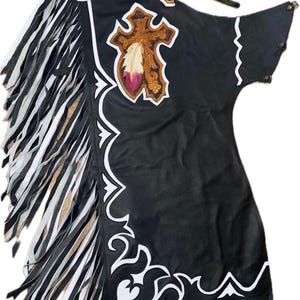 Puede incluir: Chaps de cuero negro con adornos y flecos decorativos blancos. Los chaps presentan un diseño de cuero marrón y beige con un motivo de cruz y pluma. La parte superior de los chaps tiene un diseño de cuero marrón con una figura nativa americana.