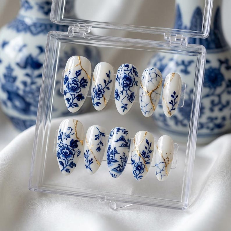 May include: A set of ten oval-shaped false nails in a clear plastic case. The nails are white with blue floral patterns and gold accents. The design resembles traditional blue and white porcelain.