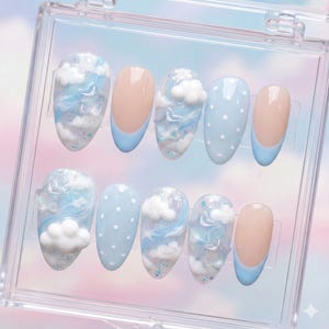 以下が含まれることがあります： 透明なプラスチックケースに入った10本のつけ爪のセット。爪には、白のドットが入った水色、水色のチップが付いたヌード、グリッターアクセント付きの雲をテーマにしたアートなど、さまざまなデザインが施されています。