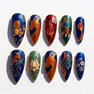 May include: A set of ten almond-shaped press-on nails featuring intricate cloisonné-style enamel designs. The artwork includes orange dragon silhouettes, floral motifs, flames, and detailed wing patterns in vibrant shades of blue, green, and red.