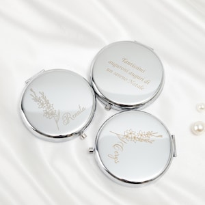 Könnte beinhalten: Drei silberne Kompaktspiegel mit floralen Designs und personalisiertem Text. Die Spiegel sind rund und haben ein glänzendes Finish. Ein Spiegel hat den Namen "Renata" eingraviert, ein anderer den Namen "Sergio", und der dritte hat Text auf Italienisch.