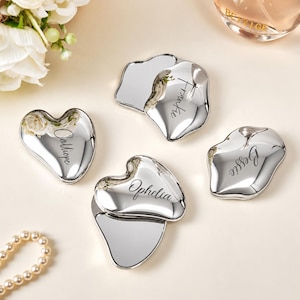 May include: Four polished silver-toned metal trinket dishes with irregular, organic shapes. Each dish is engraved with a name in a cursive script: Calliope, Frankie, Ophelia, and Bessie. The surfaces are highly reflective and smooth.