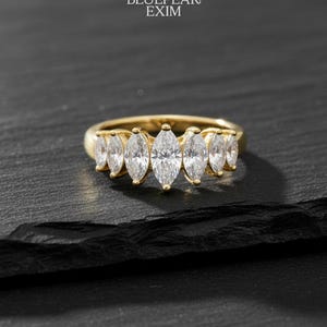 May include: A gold ring featuring seven marquise-cut diamonds. The ring is displayed on a black surface. The logo "BLUEPEAK EXIM" is visible at the top of the image.