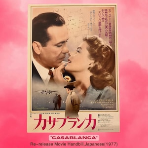 以下が含まれることがあります： ハンフリー・ボガートとイングリッド・バーグマンが出演する「カサブランカ」のヴィンテージ映画ポスター。ポスターには日本語のテキストと1977年の再公開日があります。画像は、俳優が近くにいて、背景に飛行機と人物がいます。