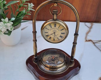 May include: A vintage brass and wood desk clock. The clock has a pocket watch design with Roman numerals and the text "VICTORIA LONDON 1876". The base features a compass design.
