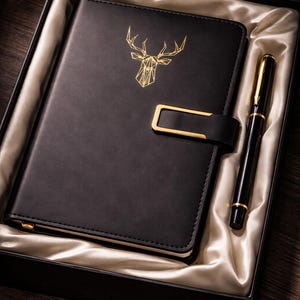 May include: A black leather journal with a gold geometric deer head design and a gold clasp, presented in a black gift box with a matching black and gold pen. The journal is nestled in a satin lining.