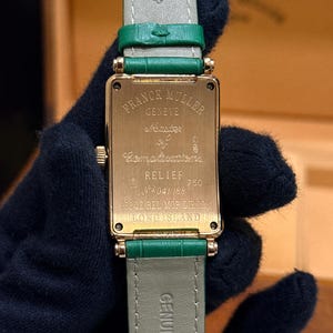 Op de afbeelding: Een gouden Franck Muller horloge met een rechthoekige wijzerplaat en een groene leren band. De wijzerplaat toont de merknaam en modeldetails. De band is groen en de woorden "Genuine Leather" zijn zichtbaar.