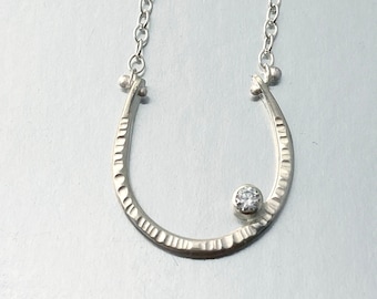 May include: A silver necklace with a textured horseshoe pendant and a single clear gemstone.