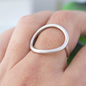 May include: A silver ring with a simple, open circle design. The ring is worn on a finger.