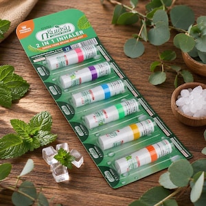 Pode incluir: Um pacote de inaladores 2 em 1 com faixas coloridas. Os inaladores são brancos com detalhes verdes e coloridos. A embalagem é verde com texto em tailandês e inglês. Folhas de hortelã fresca e cubos de gelo em primeiro plano.