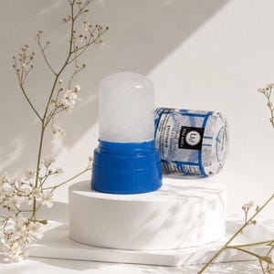 Op de afbeelding: Een doorschijnende kristallen deodorantstick met een felblauwe kunststof basis. Het productlabel bevat de tekst YOU AND I NATURAL ALUM CRYSTAL DEODORANT. De deodorant staat rechtop met de bijbehorende blauwe kunststof dop er horizontaal naast.