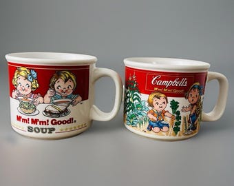 May include: Two vintage Campbell's soup mugs. Each mug features a white base with a red band at the top. One mug has illustrations of children eating soup, the other has children in a garden. Both mugs have the text "M'm! M'm! Good!"